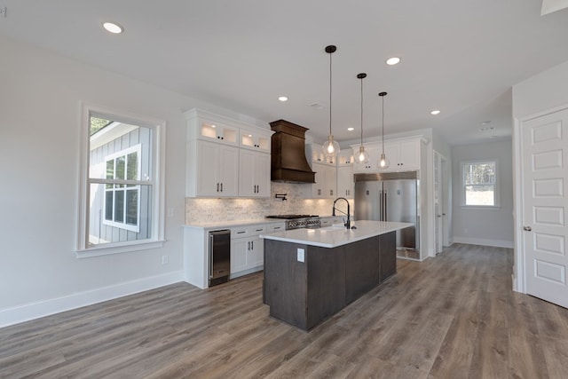 kitchen featuring white cabinetry, custom range hood, an island with sink, and hanging light fixtures