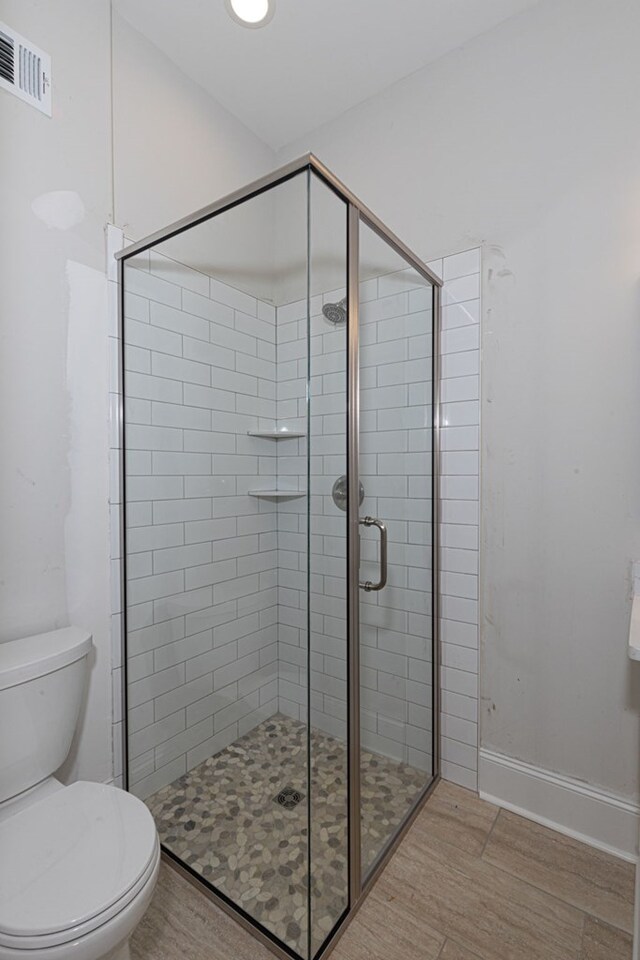 bathroom with hardwood / wood-style flooring, toilet, and a shower with shower door