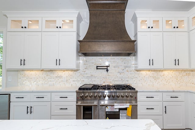 kitchen featuring premium range hood, light stone countertops, white cabinets, and appliances with stainless steel finishes