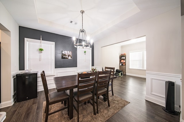 dining area with a chandelier, a tray ceiling, and dark wood-type flooring