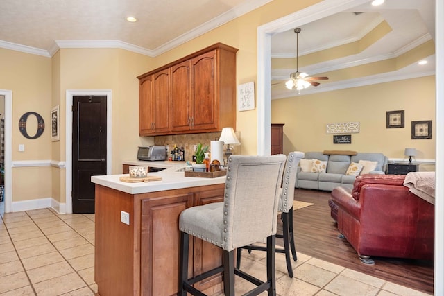 kitchen with a breakfast bar area, ornamental molding, kitchen peninsula, and ceiling fan