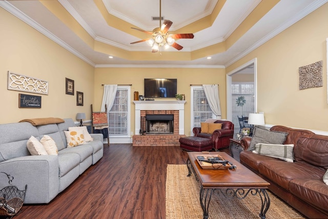 living room featuring ornamental molding, dark hardwood / wood-style floors, a tray ceiling, ceiling fan, and a fireplace