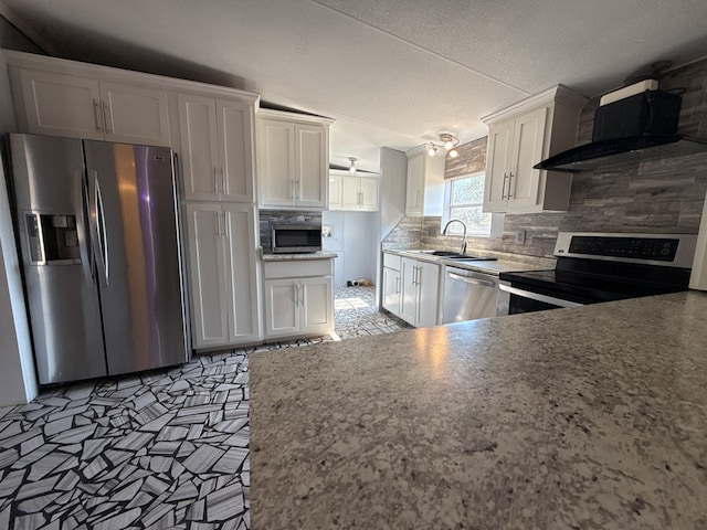 kitchen featuring tasteful backsplash, appliances with stainless steel finishes, white cabinetry, a sink, and wall chimney exhaust hood