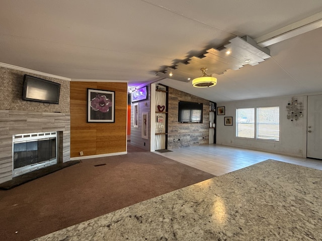 unfurnished living room with vaulted ceiling, a fireplace, carpet flooring, and wooden walls