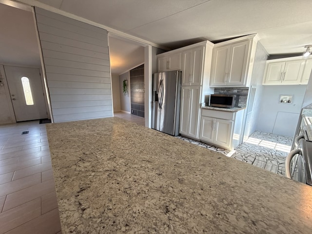 kitchen with stainless steel appliances, white cabinetry, vaulted ceiling, and light stone countertops