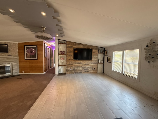 unfurnished living room featuring lofted ceiling, wood walls, a fireplace, and crown molding