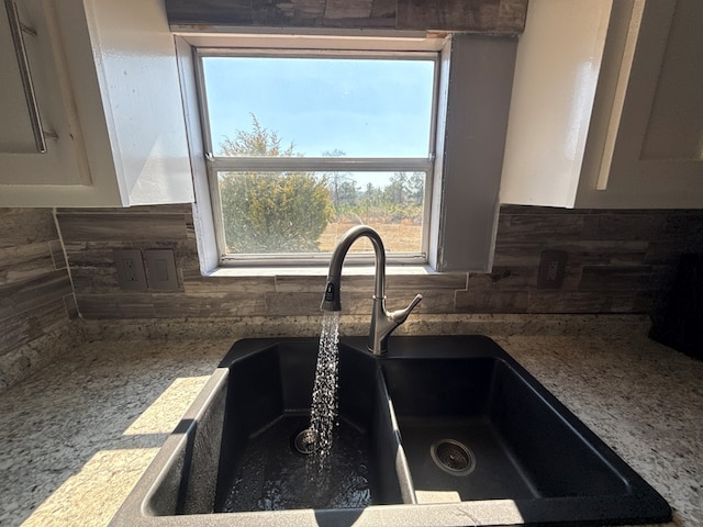 interior details featuring tasteful backsplash, stone countertops, white cabinets, and a sink