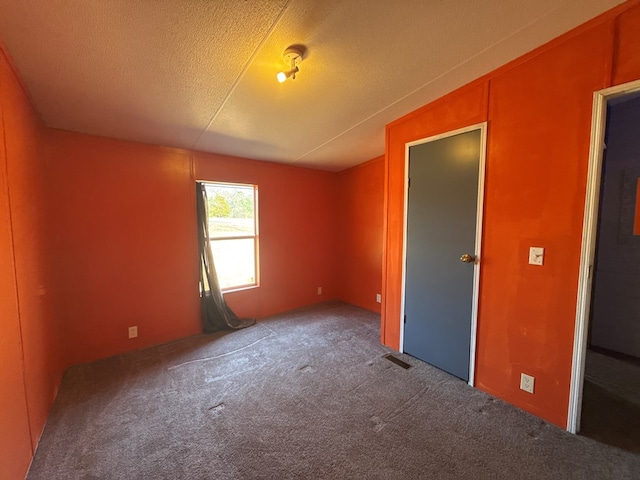 carpeted empty room featuring lofted ceiling, visible vents, and a textured ceiling