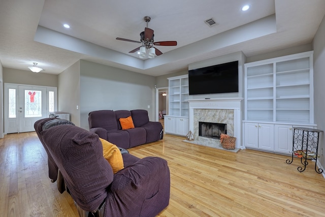 living area featuring visible vents, a fireplace, a raised ceiling, a ceiling fan, and wood-type flooring