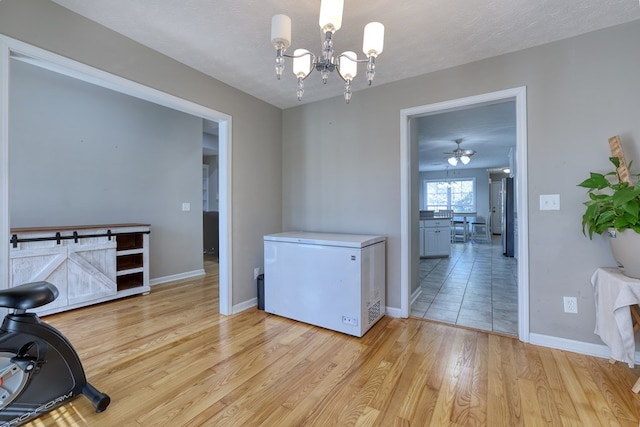 interior space featuring light wood-type flooring, baseboards, a textured ceiling, and ceiling fan with notable chandelier