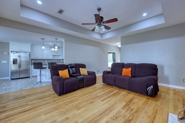 living room featuring visible vents, light wood-style flooring, a ceiling fan, and a tray ceiling