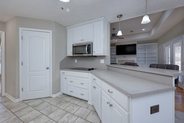 kitchen with a ceiling fan, a peninsula, white cabinetry, stainless steel microwave, and black electric stovetop