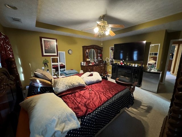 carpeted bedroom featuring a textured ceiling, a tray ceiling, fridge, and ceiling fan