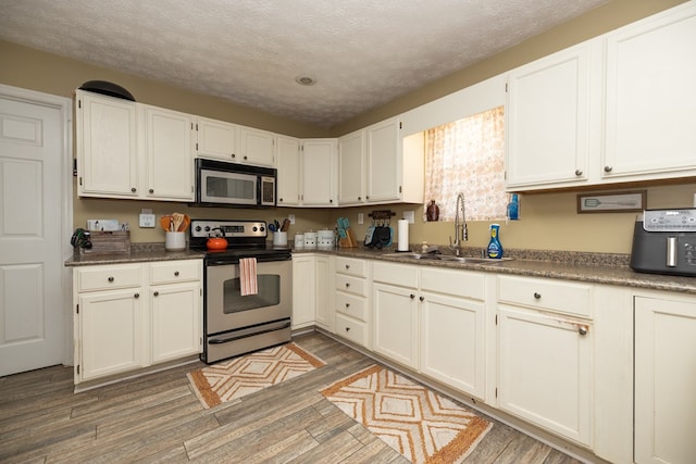 kitchen featuring dark wood-style floors, appliances with stainless steel finishes, dark countertops, and a sink