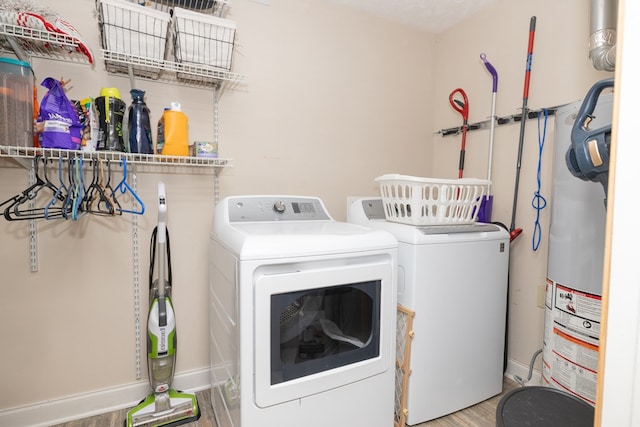 clothes washing area featuring laundry area, baseboards, wood finished floors, washing machine and dryer, and water heater