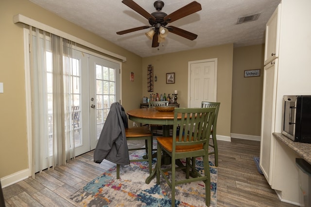 dining space with a textured ceiling, wood finished floors, visible vents, baseboards, and french doors