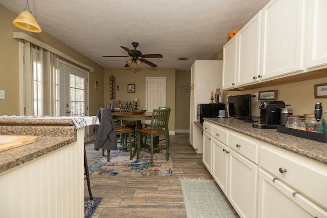 kitchen featuring a textured ceiling, light stone counters, white cabinets, dark wood-style floors, and pendant lighting