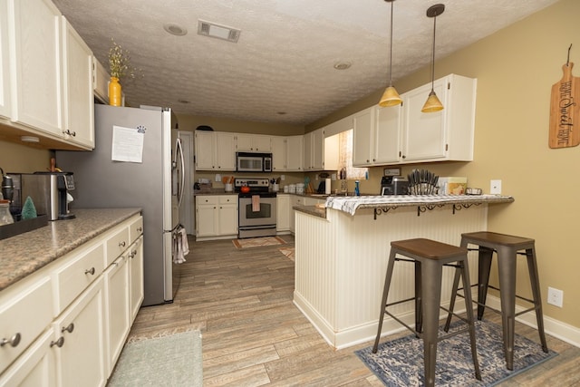 kitchen featuring a breakfast bar area, a peninsula, light wood-style floors, hanging light fixtures, and appliances with stainless steel finishes