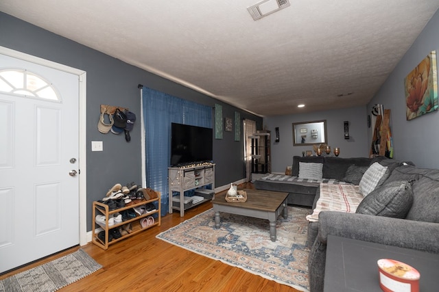 living area featuring baseboards, a textured ceiling, visible vents, and wood finished floors