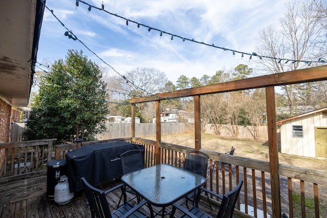 wooden terrace featuring an outbuilding, outdoor dining area, grilling area, and a fenced backyard