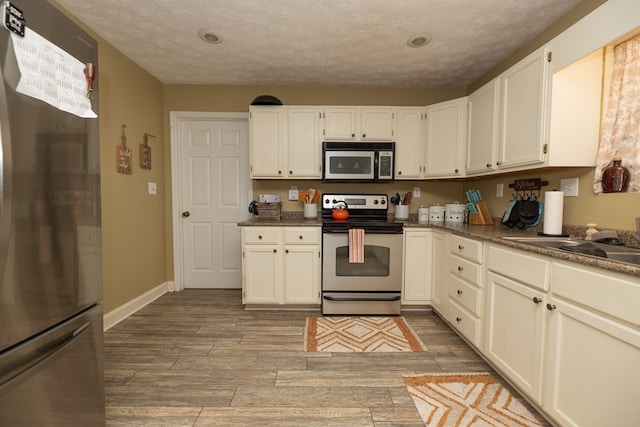 kitchen featuring dark countertops, appliances with stainless steel finishes, a textured ceiling, wood finished floors, and baseboards