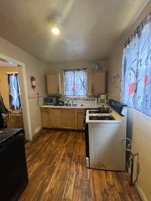 kitchen featuring white gas stove, dark wood-type flooring, tasteful backsplash, black fridge, and light brown cabinetry