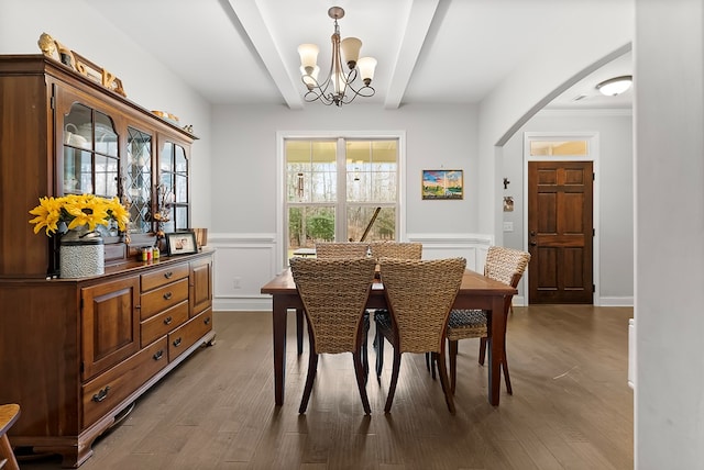 dining space featuring beam ceiling, a wainscoted wall, a notable chandelier, a decorative wall, and wood finished floors