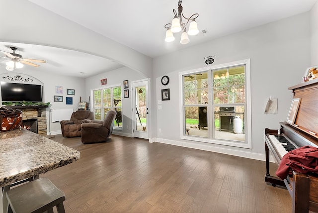 living room with arched walkways, ceiling fan with notable chandelier, dark wood-style flooring, a fireplace, and baseboards