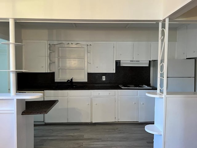 kitchen featuring dark countertops, freestanding refrigerator, white cabinetry, a sink, and under cabinet range hood