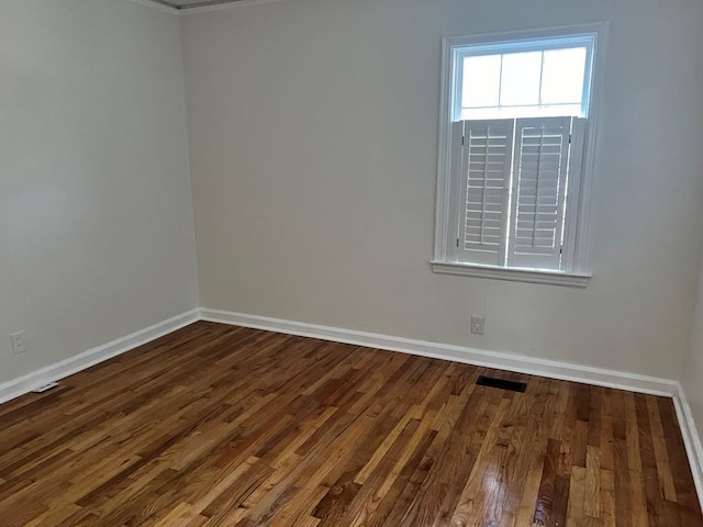 spare room with wood finished floors, visible vents, and baseboards