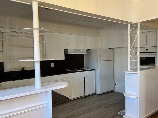 kitchen featuring white cabinets, under cabinet range hood, dark countertops, and white appliances