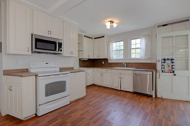 kitchen featuring appliances with stainless steel finishes, a sink, wood finished floors, and white cabinetry