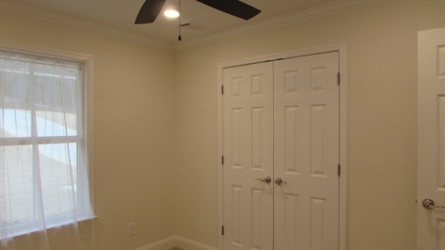 unfurnished bedroom featuring multiple windows, crown molding, a closet, and ceiling fan