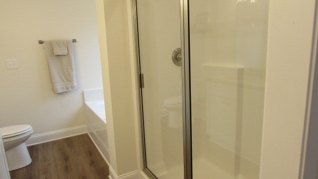 bathroom with hardwood / wood-style flooring, toilet, and plus walk in shower