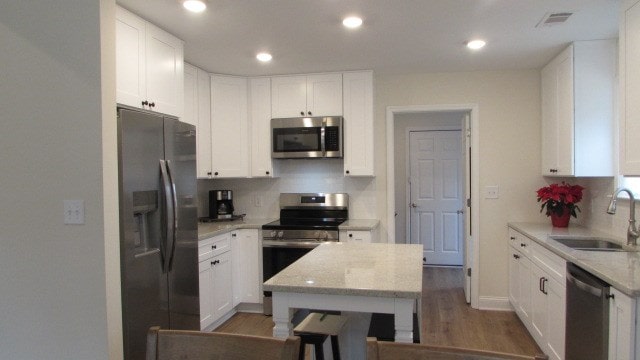 kitchen with sink, dark wood-type flooring, appliances with stainless steel finishes, white cabinetry, and light stone countertops