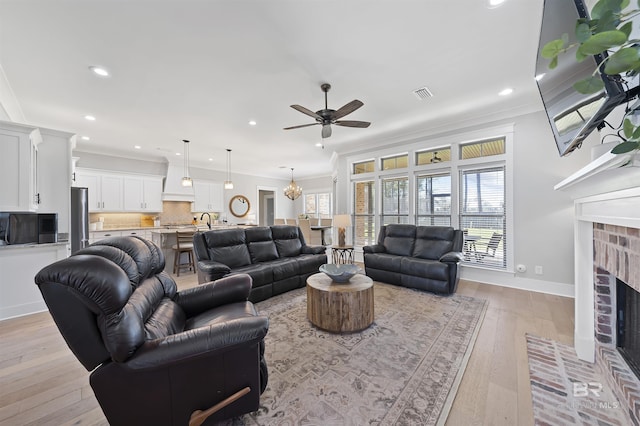 living area with ceiling fan with notable chandelier, a fireplace, visible vents, ornamental molding, and light wood-type flooring