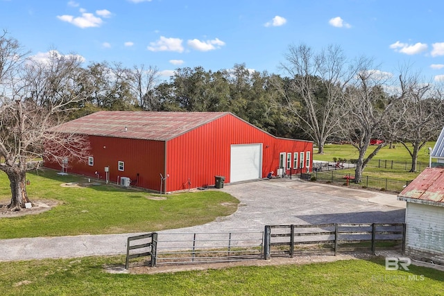 view of pole building with aphalt driveway, a lawn, and fence