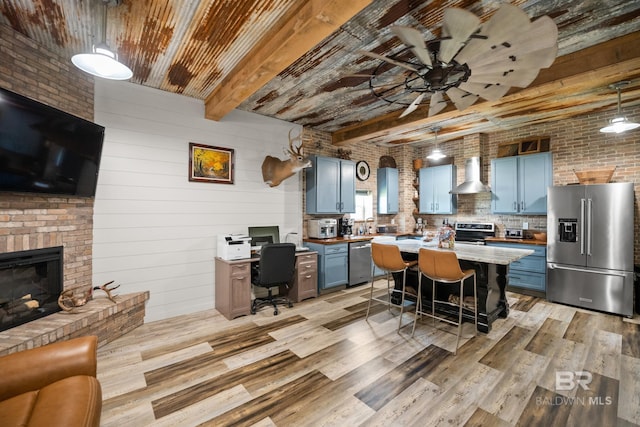 kitchen with stainless steel appliances, beamed ceiling, wall chimney range hood, and blue cabinetry