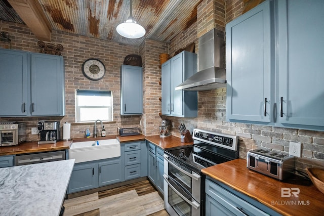 kitchen featuring range with two ovens, a sink, wall chimney exhaust hood, and wooden counters