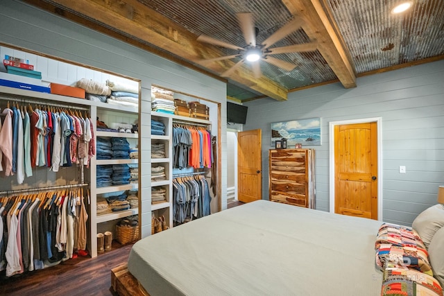 bedroom with wood walls, beamed ceiling, wood finished floors, and two closets