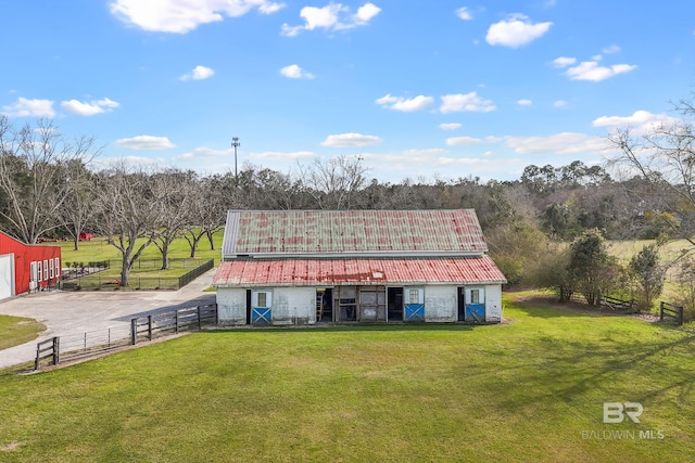 view of front of home with a barn, metal roof, an outbuilding, fence, and a front lawn