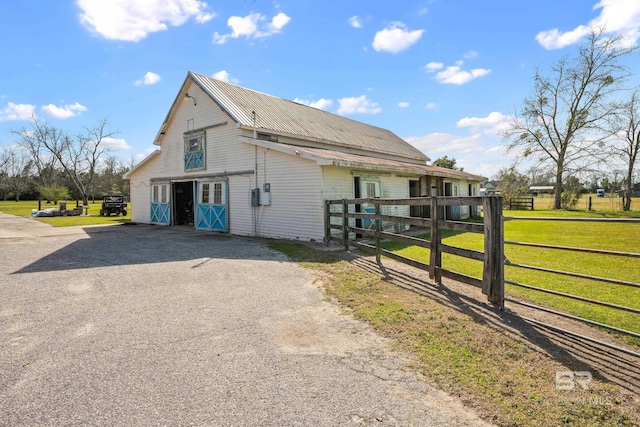 view of side of property with a yard, metal roof, driveway, and fence