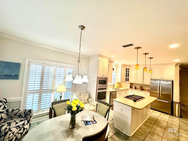 kitchen featuring appliances with stainless steel finishes, a kitchen bar, decorative light fixtures, ornamental molding, and sink