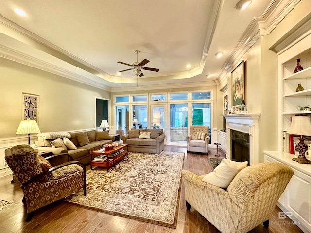 living room with a tray ceiling, hardwood / wood-style flooring, a premium fireplace, ornamental molding, and ceiling fan