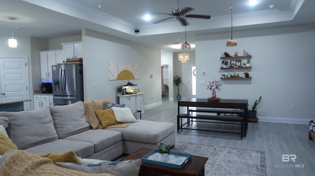 living room with a raised ceiling, ceiling fan, crown molding, and wood-type flooring