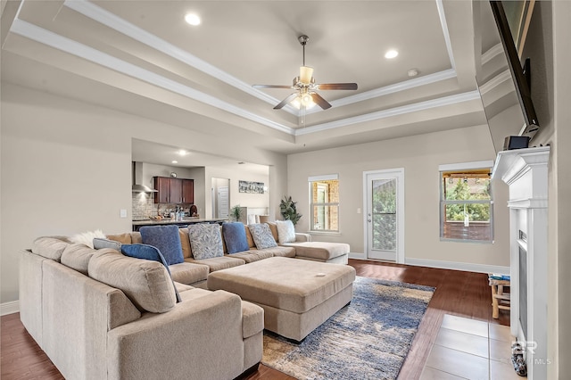 living room with ceiling fan, hardwood / wood-style flooring, a raised ceiling, and ornamental molding