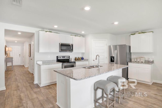 kitchen with appliances with stainless steel finishes, light stone counters, a kitchen island with sink, sink, and white cabinets