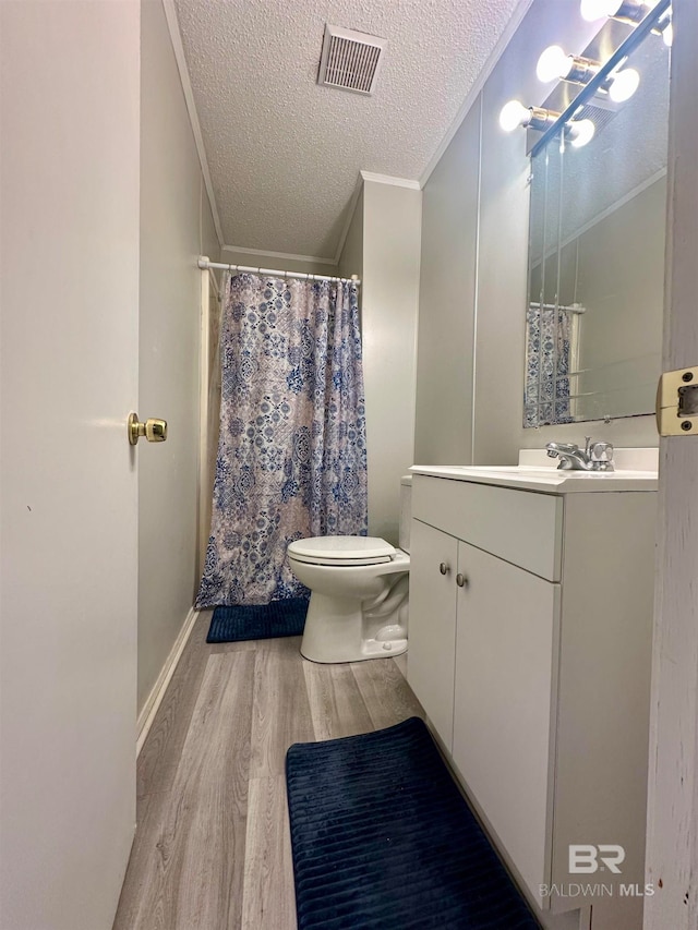 bathroom featuring wood-type flooring, a textured ceiling, toilet, vanity, and ornamental molding