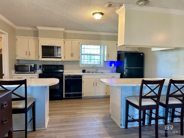 kitchen featuring a kitchen bar, sink, black appliances, and light hardwood / wood-style flooring