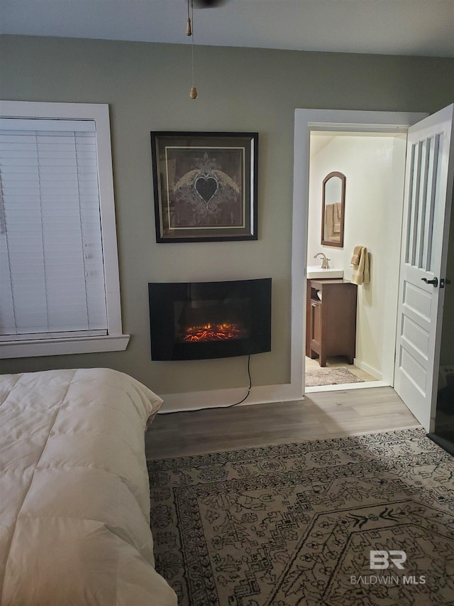 bedroom with ensuite bathroom, baseboards, a glass covered fireplace, and wood finished floors